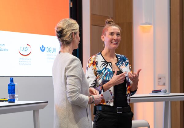 Moderatorin Corinna Lampadius und Keynote-Speakerin Dr. Stefanie Schöler unterhalten sich auf der Bühne beim "Dialog Zukunft Arbeitsschutz 2025"